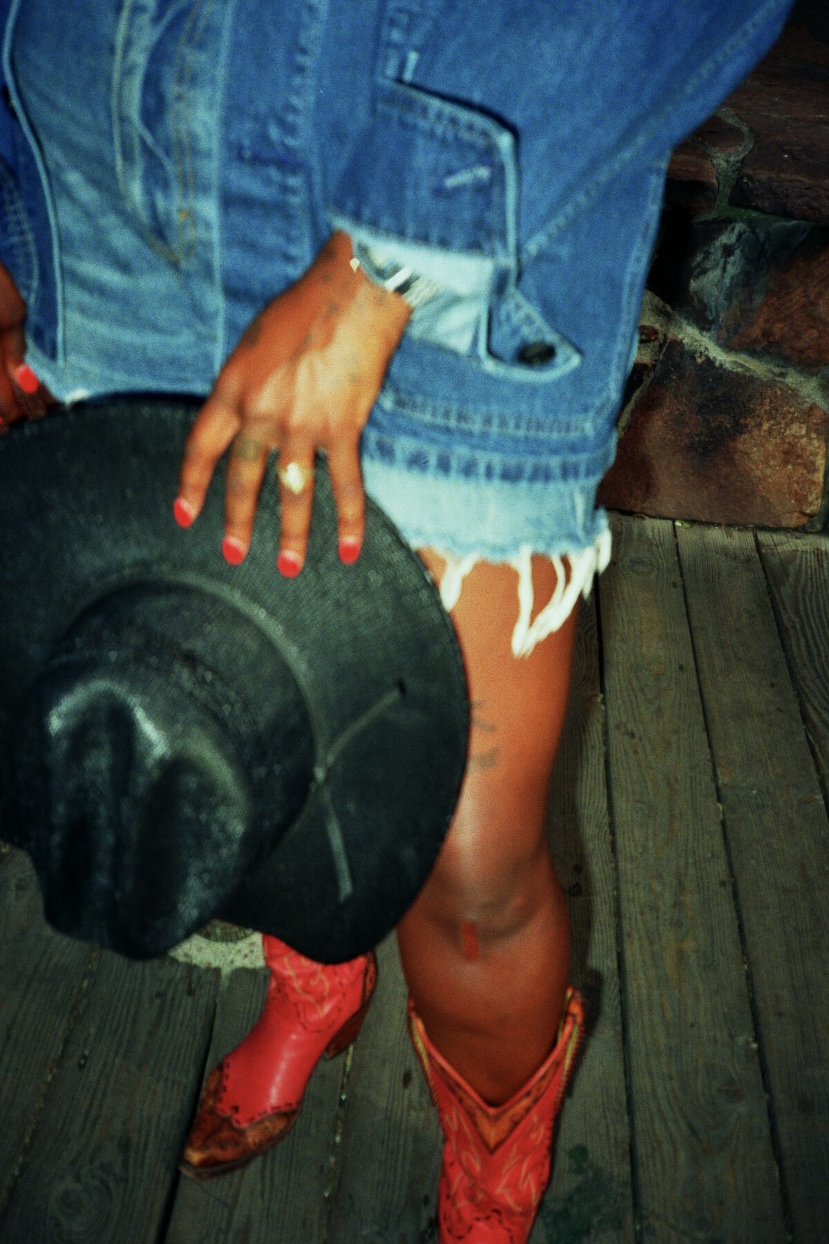 Denim, a black hat held low, red boots on a boardwalk
